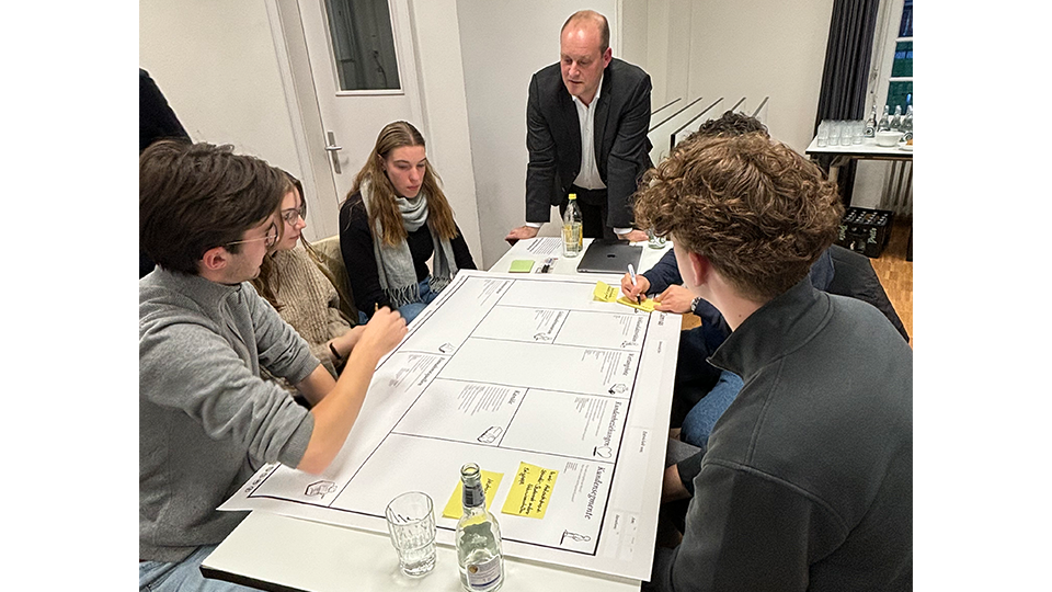 Gruppe von Studierenden gemeinsam mit apetito Mitarbeiter David Baller über ein Worksheet geneigt